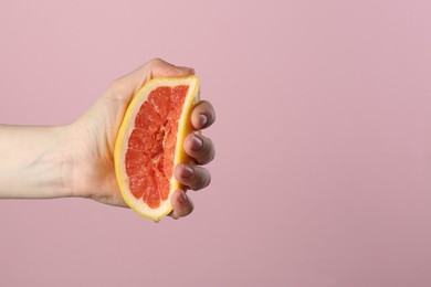 Photo of Woman squeezing grapefruit on pink background, closeup. Space for text