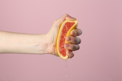 Photo of Woman squeezing grapefruit on pink background, closeup