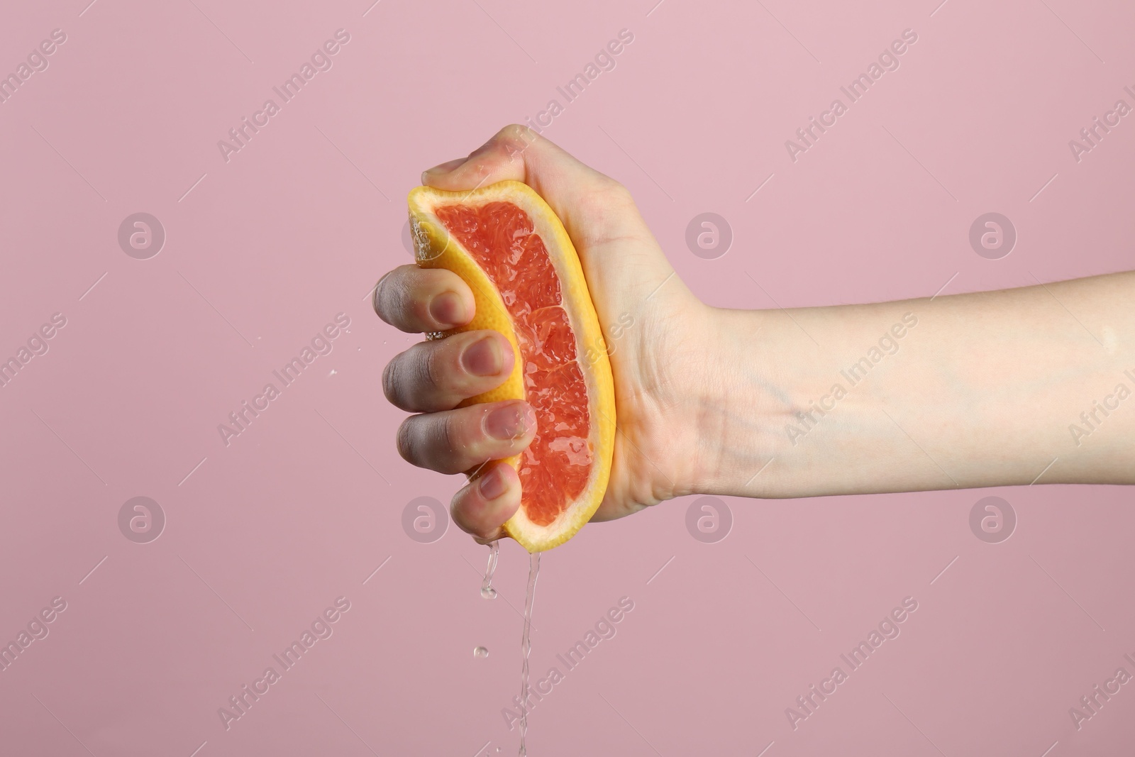 Woman squeezing grapefruit on pink background, closeup Photo of Woman squeezing grapefruit on pink background, closeup