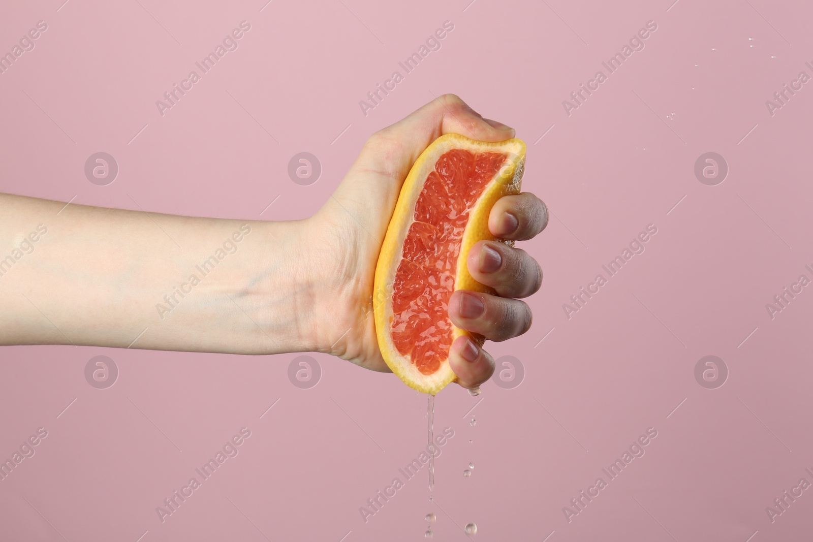 Woman squeezing grapefruit on pink background, closeup Photo of Woman squeezing grapefruit on pink background, closeup