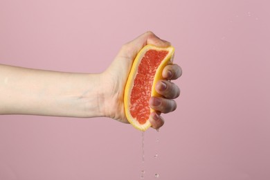 Photo of Woman squeezing grapefruit on pink background, closeup