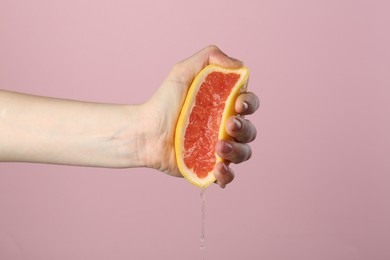 Photo of Woman squeezing grapefruit on pink background, closeup