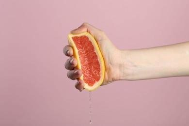Photo of Woman squeezing grapefruit on pink background, closeup