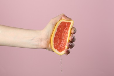 Photo of Woman squeezing grapefruit on pink background, closeup