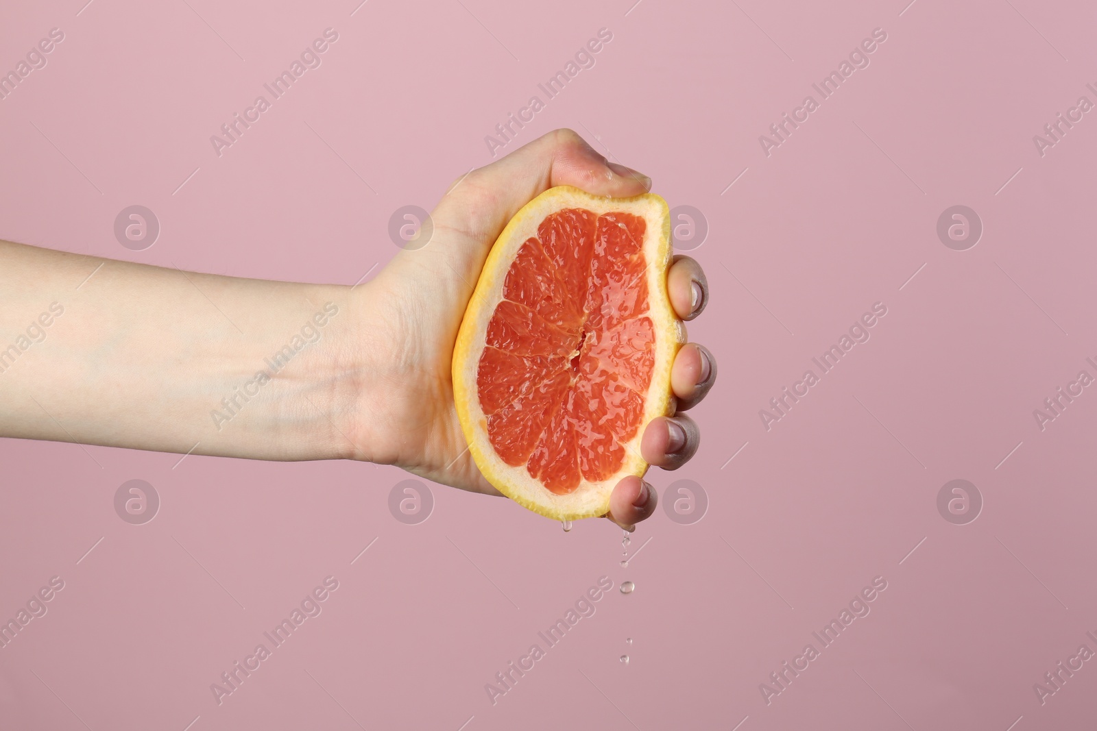 Woman squeezing grapefruit on pink background, closeup Photo of Woman squeezing grapefruit on pink background, closeup