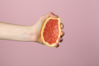 Photo of Woman squeezing grapefruit on pink background, closeup