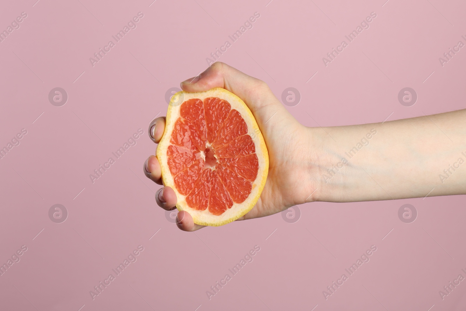 Woman squeezing grapefruit on pink background, closeup Photo of Woman squeezing grapefruit on pink background, closeup