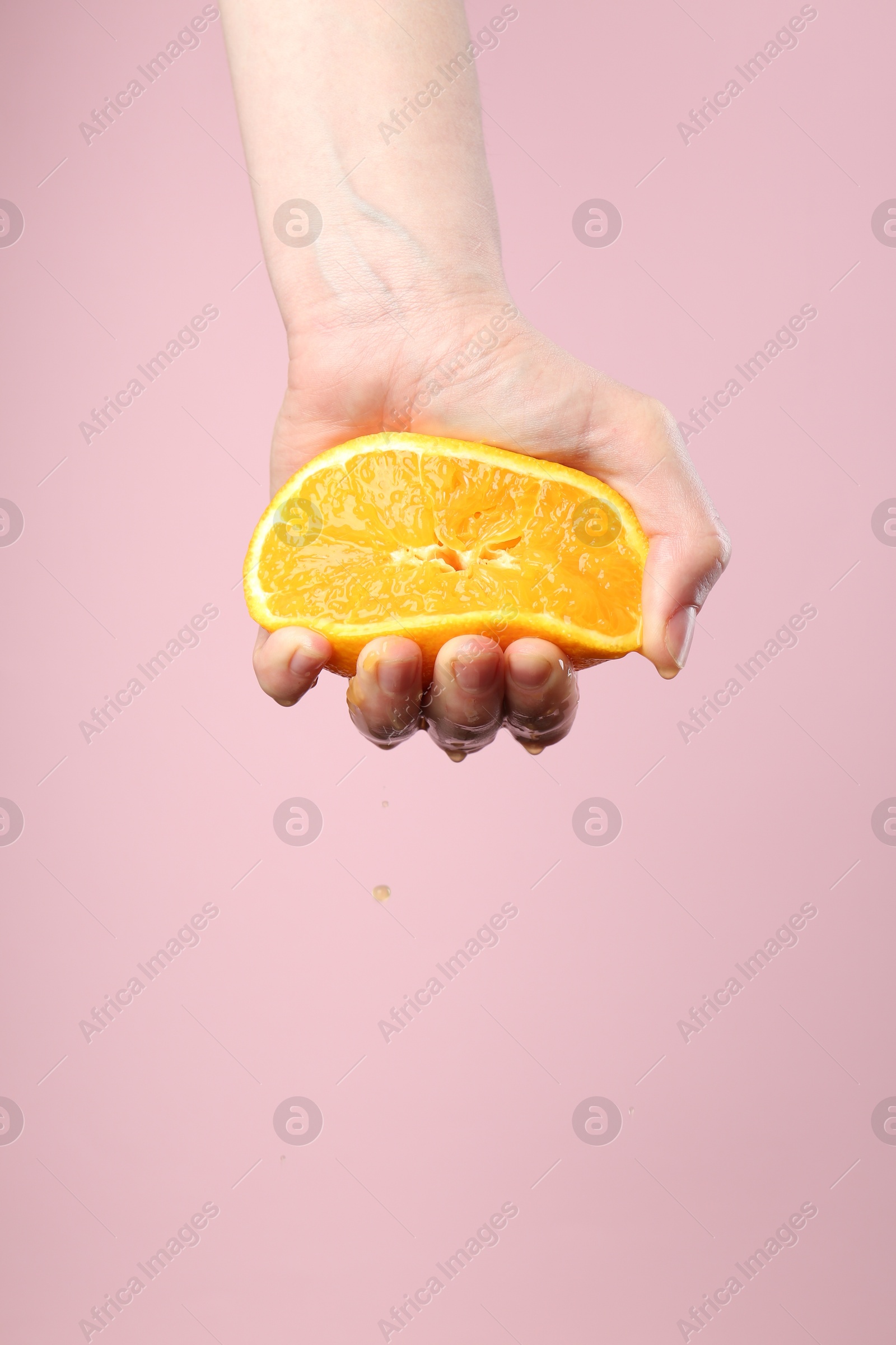Woman squeezing orange on pink background, closeup. Space for text Photo of Woman squeezing orange on pink background, closeup. Space for text