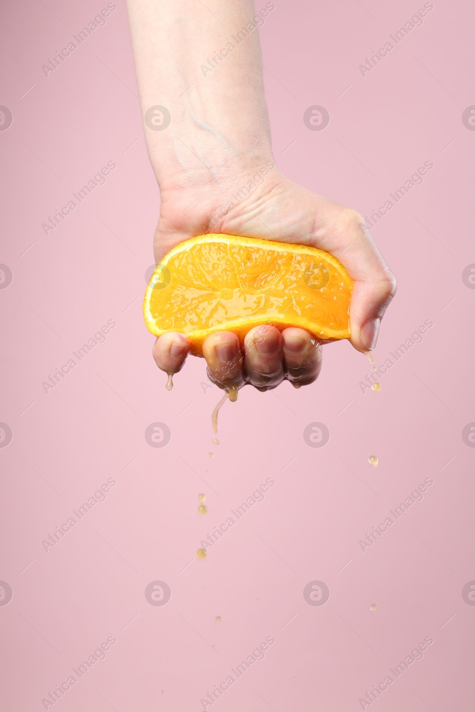 Woman squeezing orange on pink background, closeup. Space for text Photo of Woman squeezing orange on pink background, closeup. Space for text