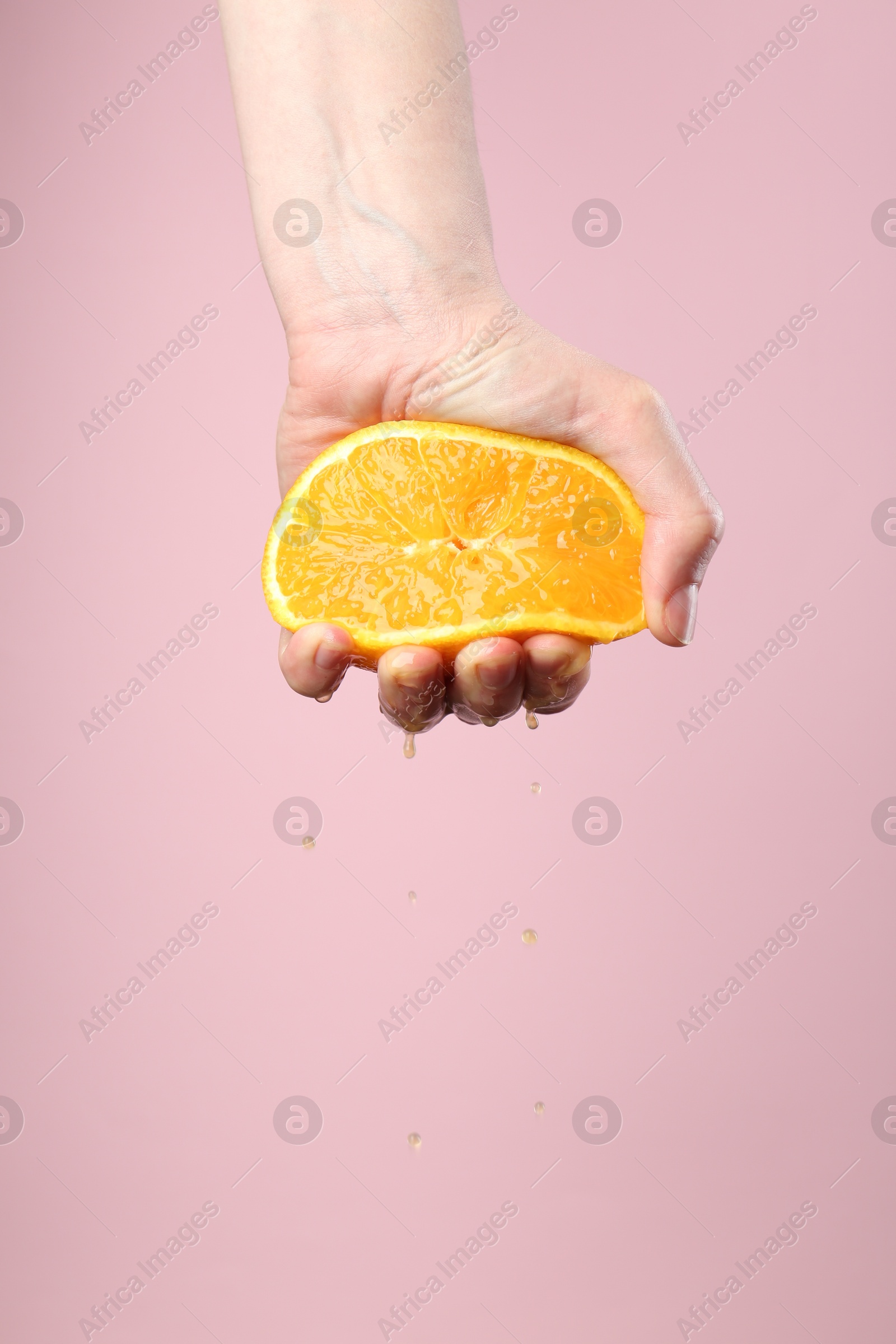 Woman squeezing orange on pink background, closeup. Space for text Photo of Woman squeezing orange on pink background, closeup. Space for text