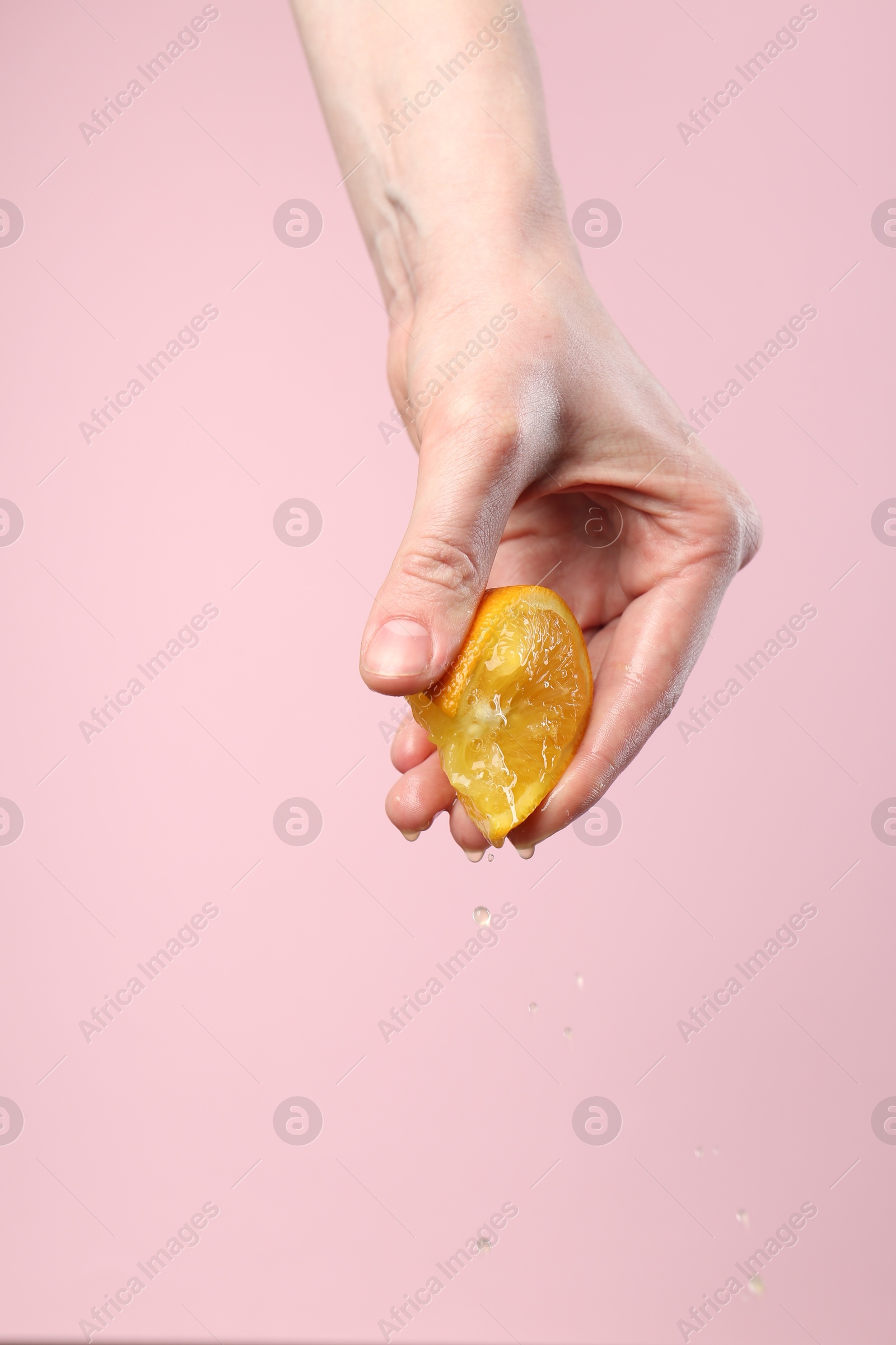 Woman squeezing orange on pink background, closeup. Space for text Photo of Woman squeezing orange on pink background, closeup. Space for text