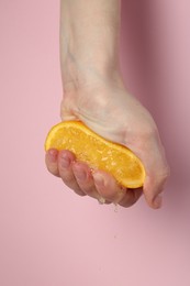 Photo of Woman squeezing orange on pink background, closeup