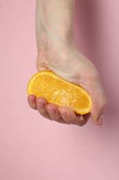 Photo of Woman squeezing orange on pink background, closeup