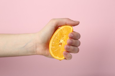 Photo of Woman squeezing orange on pink background, closeup