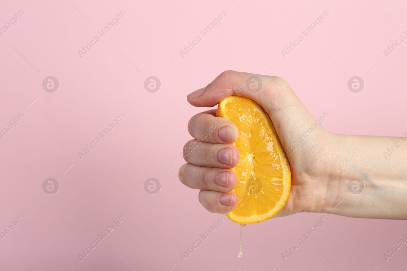 Woman squeezing orange on pink background, closeup Photo of Woman squeezing orange on pink background, closeup