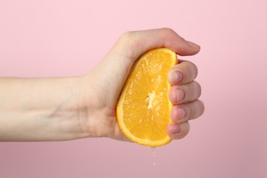 Photo of Woman squeezing orange on pink background, closeup