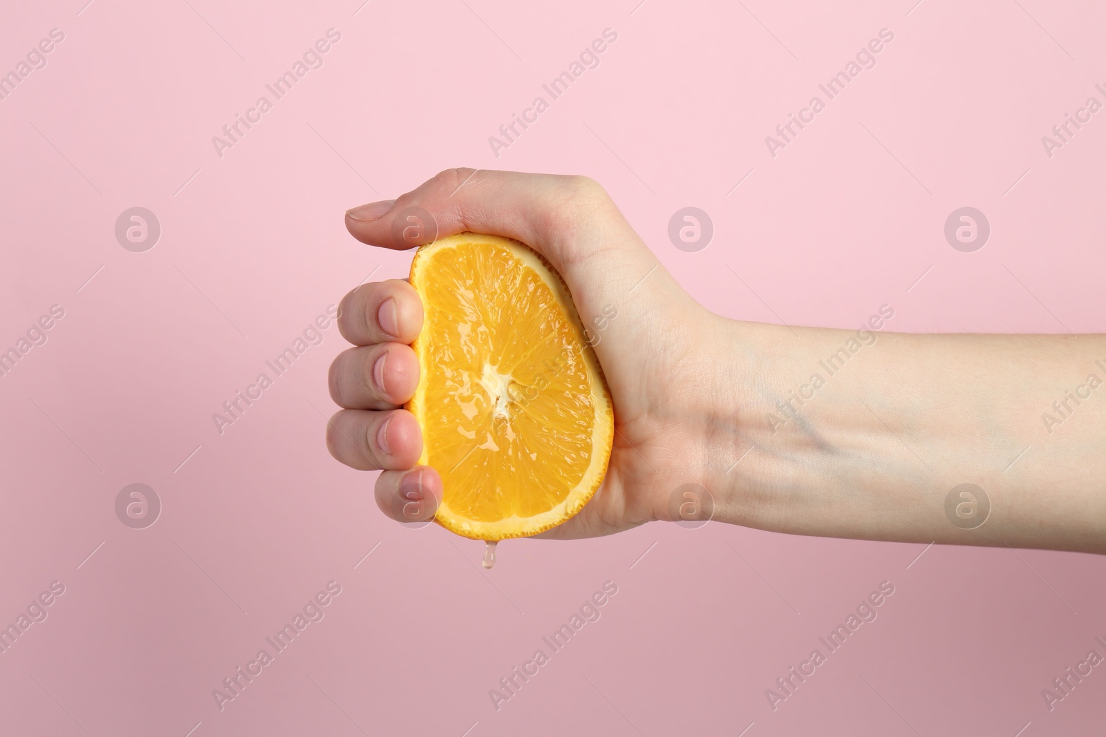 Woman squeezing orange on pink background, closeup Photo of Woman squeezing orange on pink background, closeup