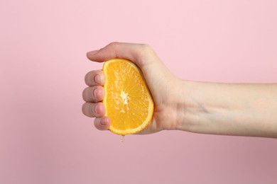Photo of Woman squeezing orange on pink background, closeup