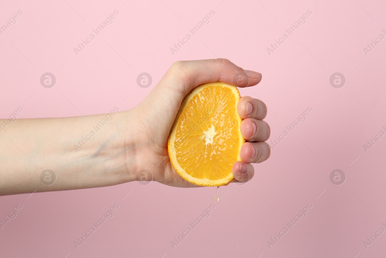 Woman squeezing orange on pink background, closeup Photo of Woman squeezing orange on pink background, closeup