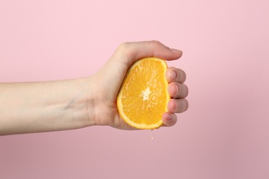 Photo of Woman squeezing orange on pink background, closeup