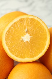 Photo of Half of fresh orange among whole ones on blurred light background, closeup