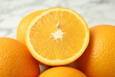 Photo of Half of fresh orange among whole ones on blurred light background, closeup