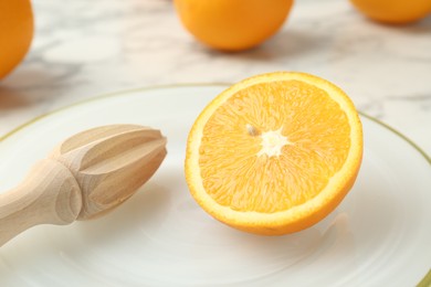 Photo of Half of fresh orange and squeezer on white marble table, closeup
