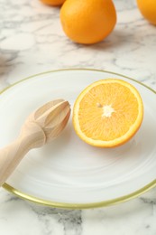 Photo of Half of fresh orange and squeezer on white marble table, closeup