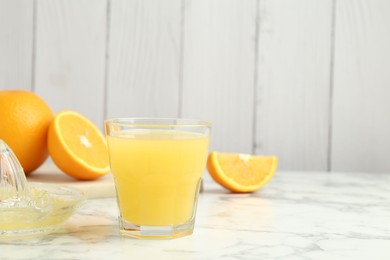Photo of Fresh orange juice, fruits and squeezer on white marble table against wooden background, closeup. Space for text