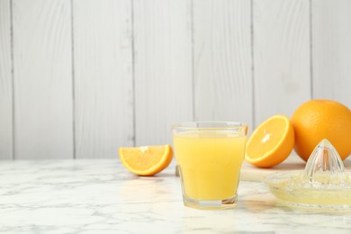 Photo of Fresh orange juice, fruits and squeezer on white marble table against wooden background, closeup. Space for text