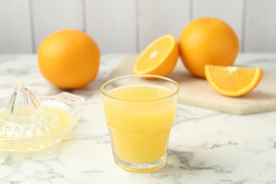 Photo of Fresh orange juice, fruits and squeezer on white marble table, closeup