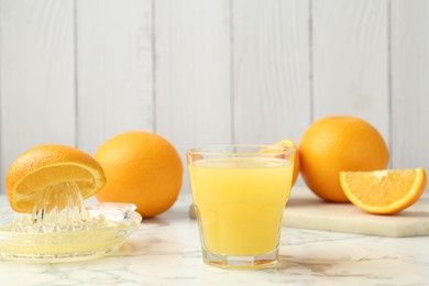 Photo of Fresh orange juice, fruits and squeezer on white marble table against wooden background, closeup