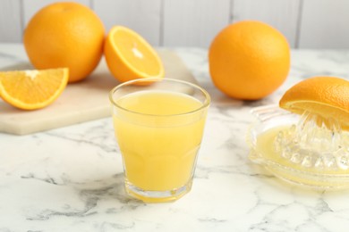 Photo of Fresh orange juice, fruits and squeezer on white marble table, closeup