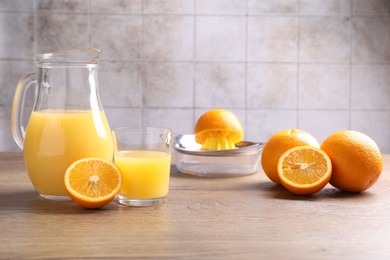 Photo of Fresh orange juice, fruits and squeezer on wooden table against grey tiled wall, closeup