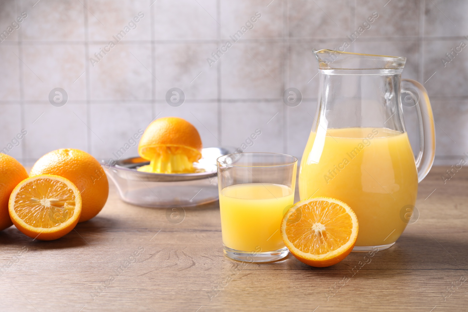 Fresh orange juice, fruits and squeezer on wooden table against grey tiled wall, closeup Photo of Fresh orange juice, fruits and squeezer on wooden table against grey tiled wall, closeup