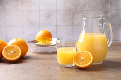 Photo of Fresh orange juice, fruits and squeezer on wooden table against grey tiled wall, closeup