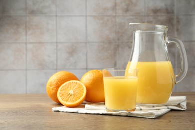 Photo of Fresh orange juice and fruits on wooden table against grey tiled wall