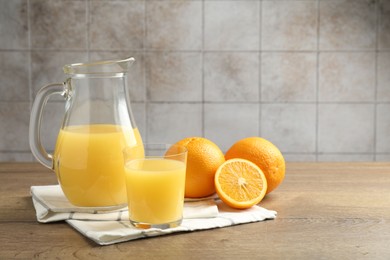 Photo of Fresh orange juice and fruits on wooden table against grey tiled wall