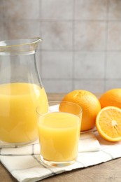Photo of Fresh orange juice and fruits on wooden table against grey tiled wall, closeup