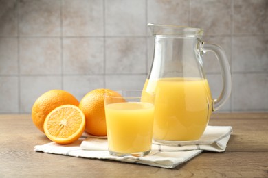 Photo of Fresh orange juice and fruits on wooden table against grey tiled wall, closeup