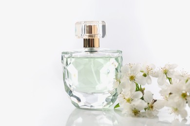 Photo of Aromatic perfume and beautiful flowers on white background, closeup