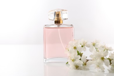 Photo of Aromatic perfume and beautiful flowers on white background, closeup