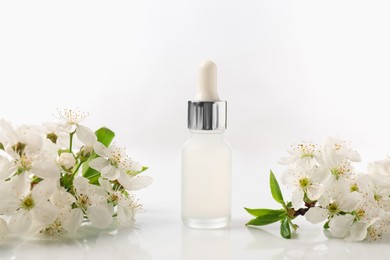 Photo of Bottle of cosmetic product and beautiful flowers on white background, closeup