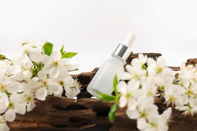 Photo of Bottle of cosmetic product, tree bark and beautiful flowers on white background, closeup