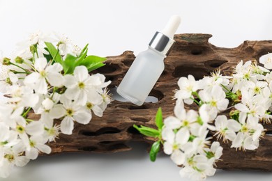 Photo of Bottle of cosmetic product, tree bark and beautiful flowers on white background, closeup