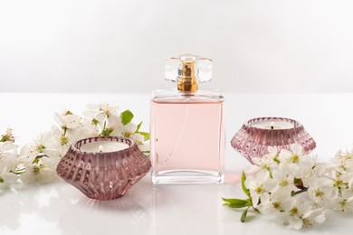 Photo of Aromatic perfume, burning candles and beautiful flowers on white background, closeup