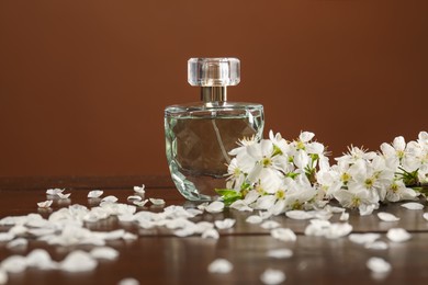 Photo of Aromatic perfume and beautiful flowers on wooden table, closeup