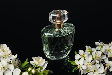 Photo of Aromatic perfume and beautiful flowers on black mirror surface, closeup