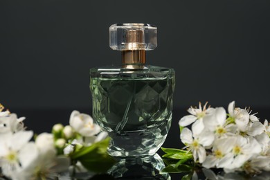 Photo of Aromatic perfume and beautiful flowers on black mirror surface, closeup