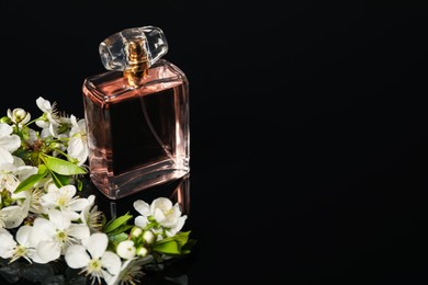 Photo of Aromatic perfume and beautiful flowers on black mirror surface, closeup. Space for text
